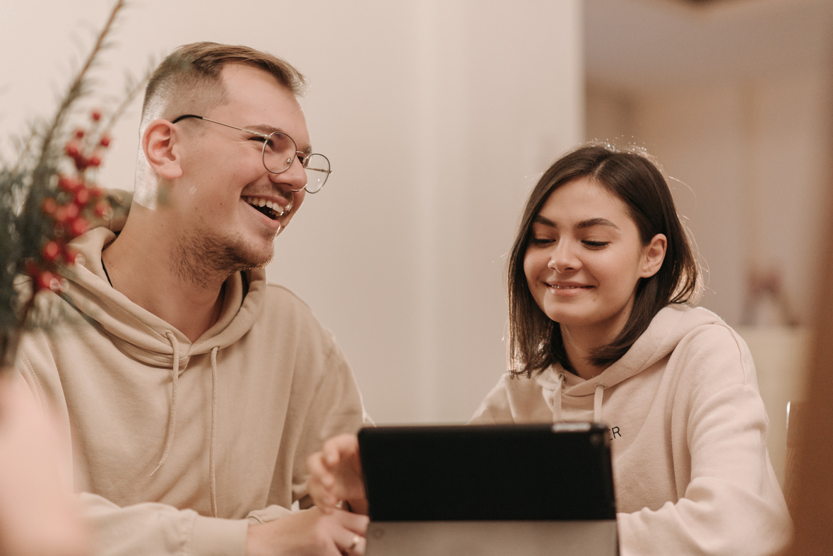 Man and Woman in Beige Hoodie Laughing In Front of an iPad 